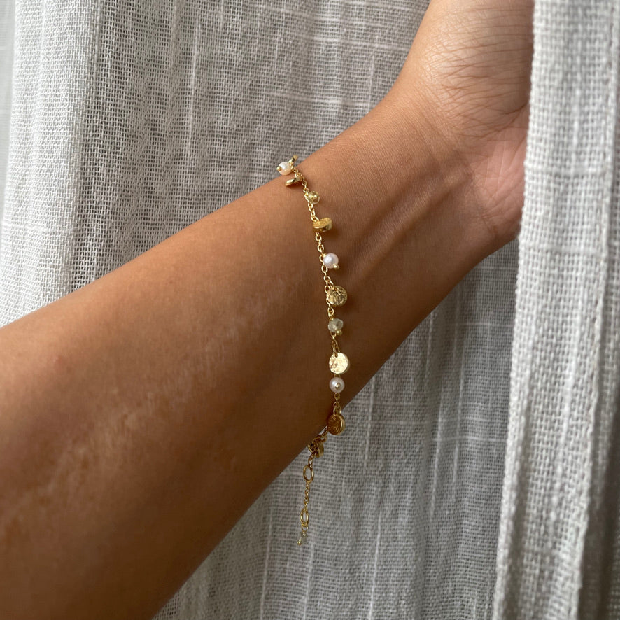 Gold bracelet with pearls on a wrist against a neutral background