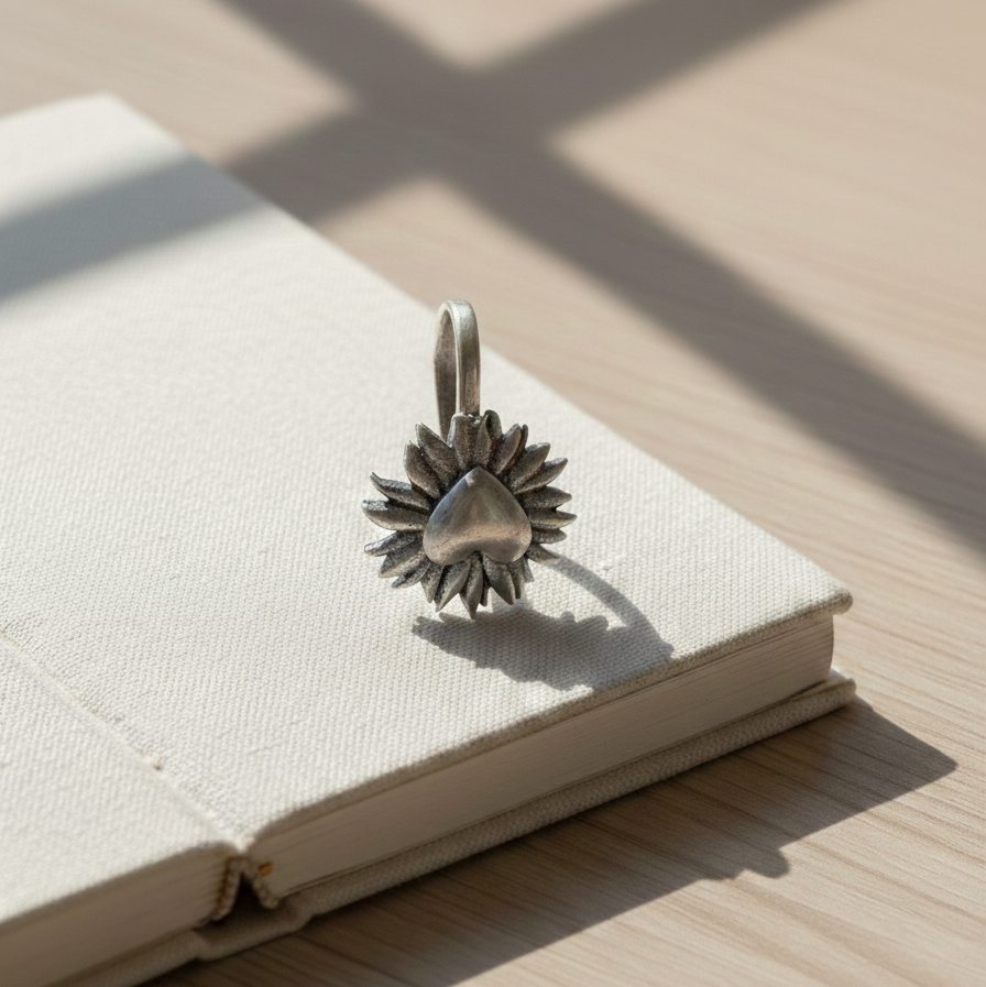 An artistic shot of an oxidized silver, petal-framed heart facial ornament resting on an open book, bathed in natural sunlight.