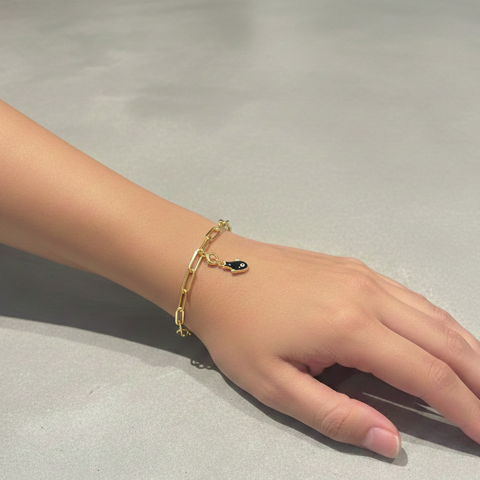 A close-up view of a wrist wearing a delicate gold link chain bracelet adorned with a small, navy blue enamel fish-shaped pendant featuring a centered white eye design.