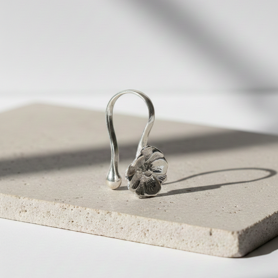 Silver Peony Nose Clip featuring a sculpted floral design with curved hook style, displayed on a neutral stone surface in soft natural light.
