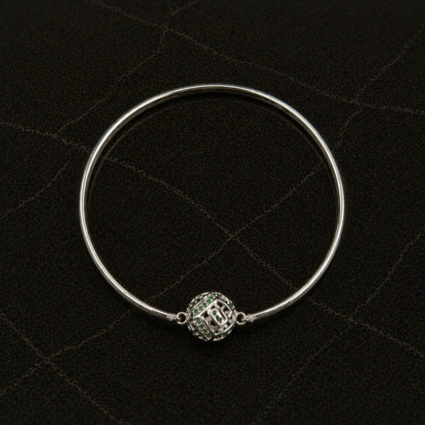 Top-down flat lay of the handcrafted Green Glow Rolling Bangle in rhodium-plated brass featuring a centered sphere with green CZ stones.