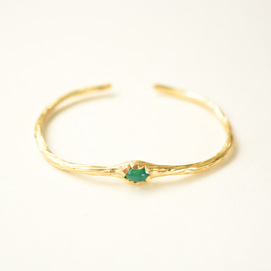 Gold bracelet with a green gemstone on a white background