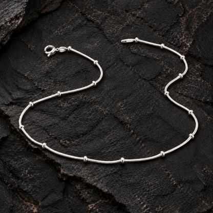 Silver anklet with spaced beads on a dark textured rock surface
