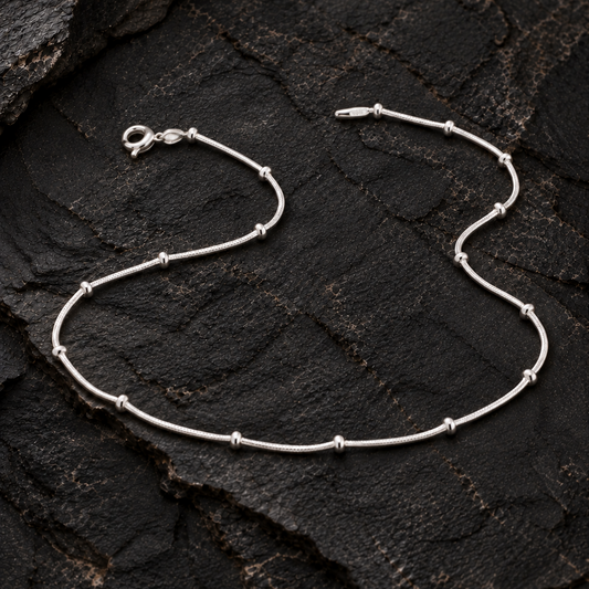 Silver anklet with spaced beads on a dark textured rock surface