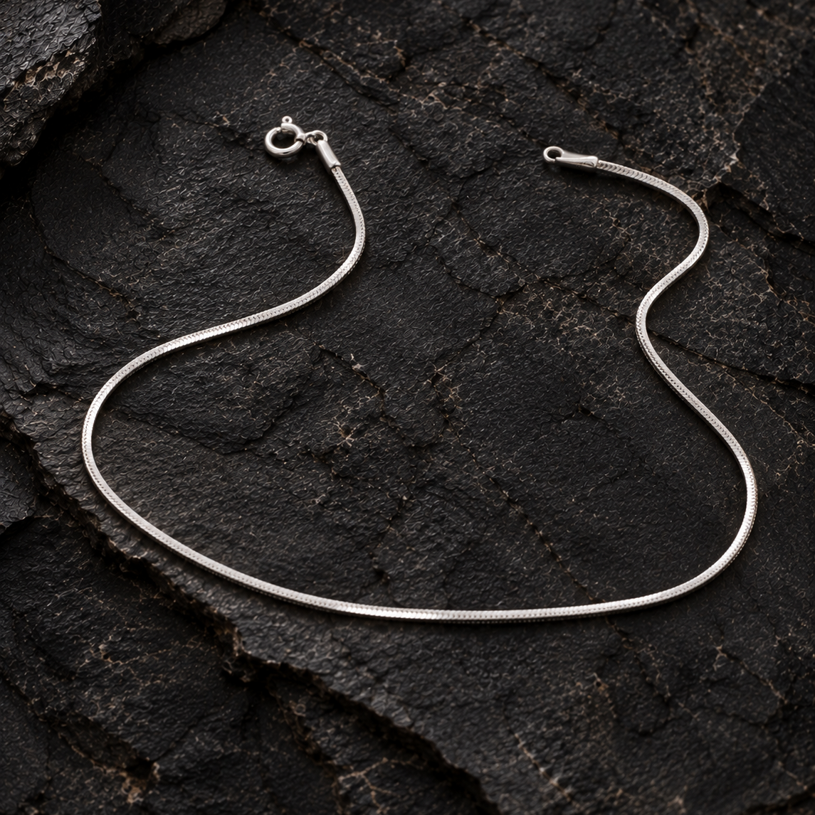 Silver snake chain anklet on a dark textured rock surface