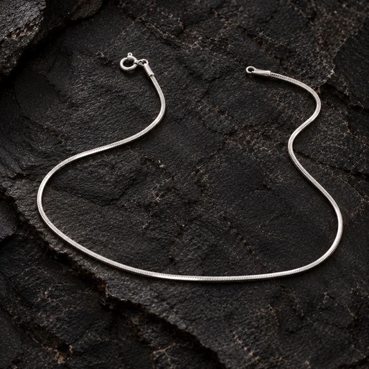 Silver snake chain anklet on a dark textured rock surface
