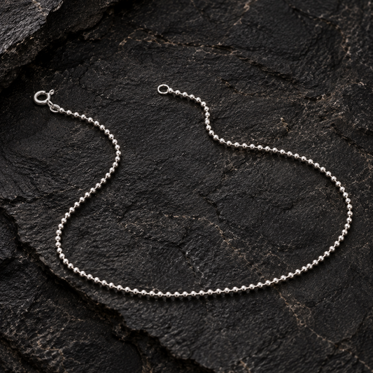 Silver beaded anklet on a dark textured rock surface