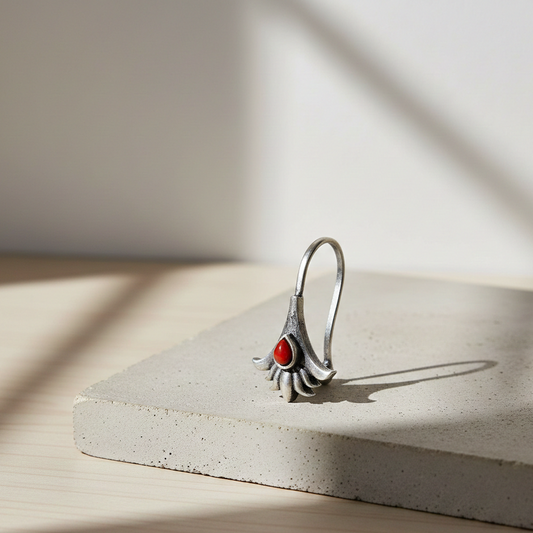 Carnelian Blossom Clip-On nose jewelry featuring a silver floral design with a teardrop-shaped red carnelian stone, displayed on a light stone pedestal in warm natural light.