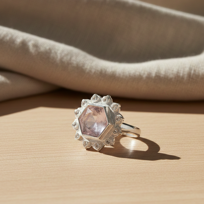 Celestial Blush Ring with a faceted hexagon gemstone in a detailed silver halo setting on a wooden surface.