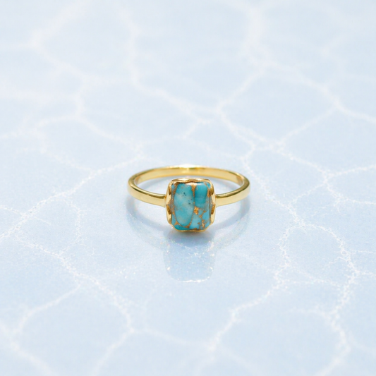Front view of the Earth Harmony Ring featuring a rectangular copper turquoise stone with natural blue and copper tones on a light blue textured surface.