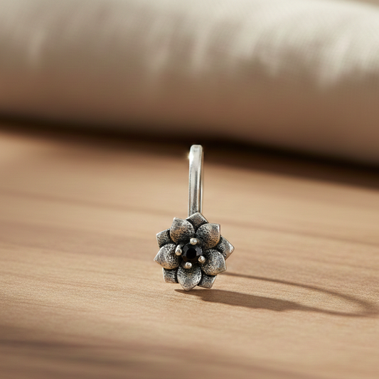 Silver floral clip-on earring with a dark amethyst center stone displayed on a warm wooden surface in soft light.