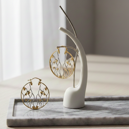 Entangled Hoop Earrings featuring round gold hoops with intricate silver vine detailing, displayed on a marble tray with a modern jewelry stand in soft natural light.