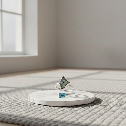 Ethereal Ring in silver featuring an organic triangular iridescent inlay, displayed on a white marble pedestal with soft natural window light.