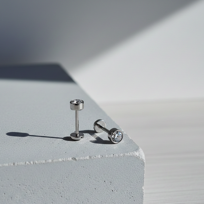 Minimal silver flat back stud earring with round clear gemstone displayed on a concrete block in soft natural light.