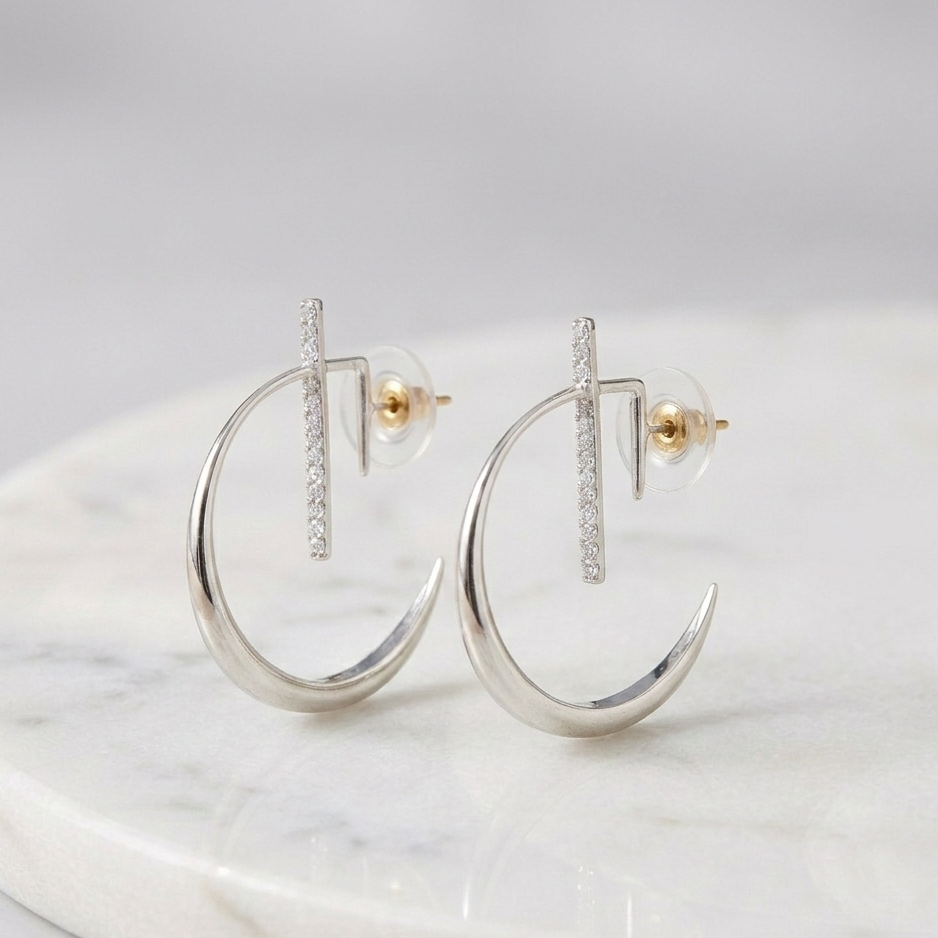 A pair of La Luna Platinum Earrings featuring a sleek, high-polished crescent moon hoop design intersected by a vertical bar set with shimmering pavé diamonds, displayed on a white marble surface.