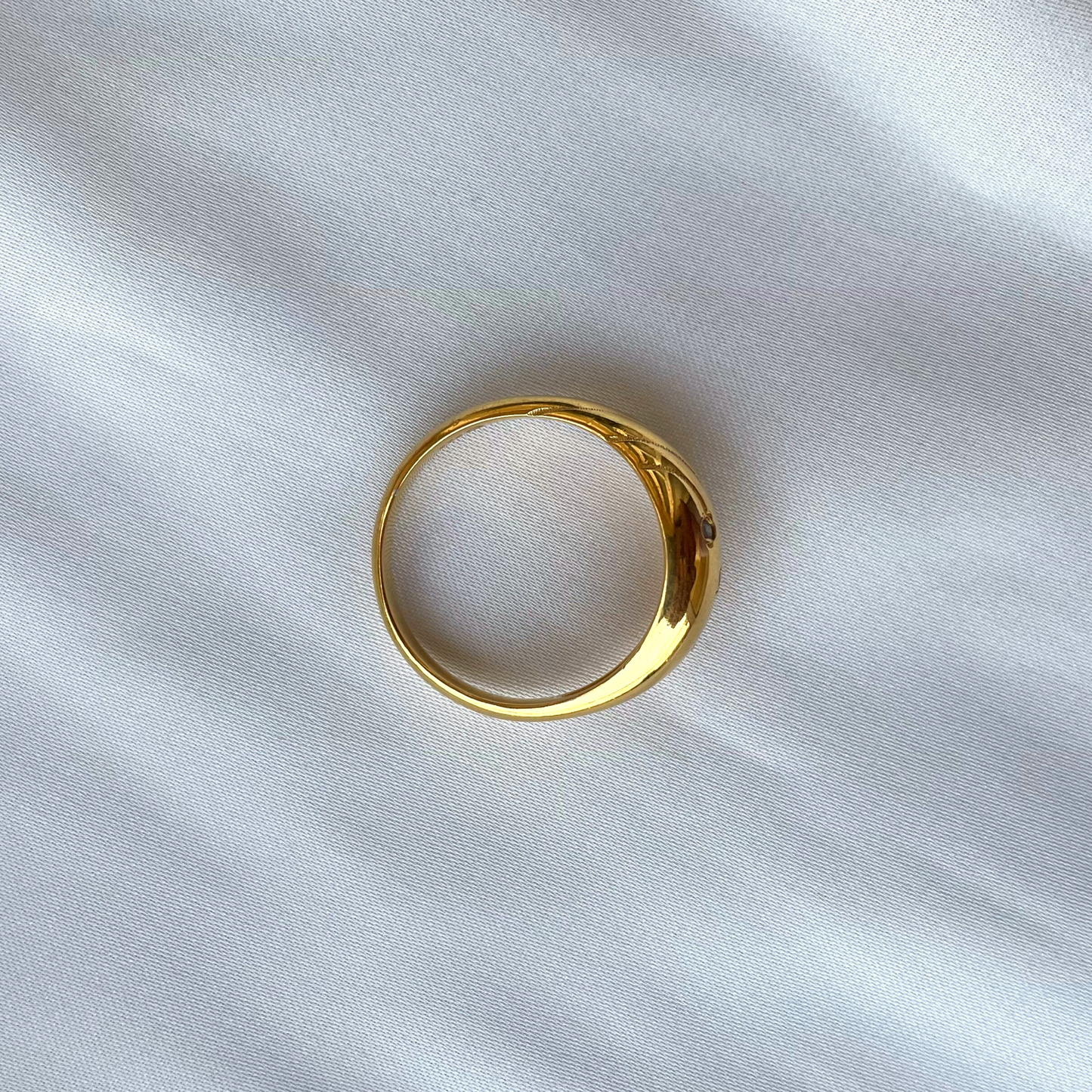A top-down view of a thick, polished gold band ring set against a clean, white fabric backdrop.