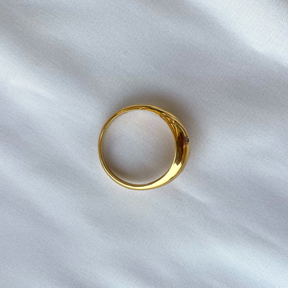 A top-down view of a thick, polished gold band ring set against a clean, white fabric backdrop.