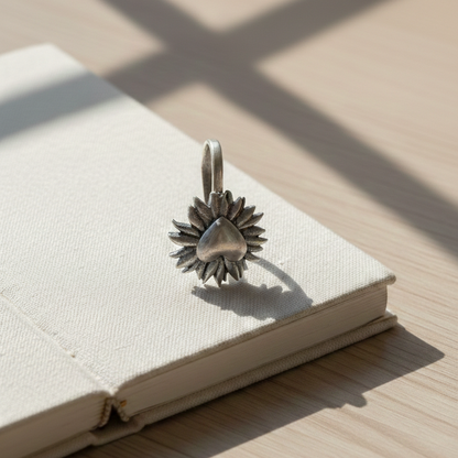 An artistic shot of an oxidized silver, petal-framed heart facial ornament resting on an open book, bathed in natural sunlight.