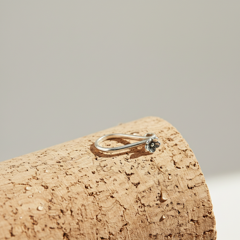 A dainty silver floral nose clip resting on a textured, light brown cylindrical cork surface.
