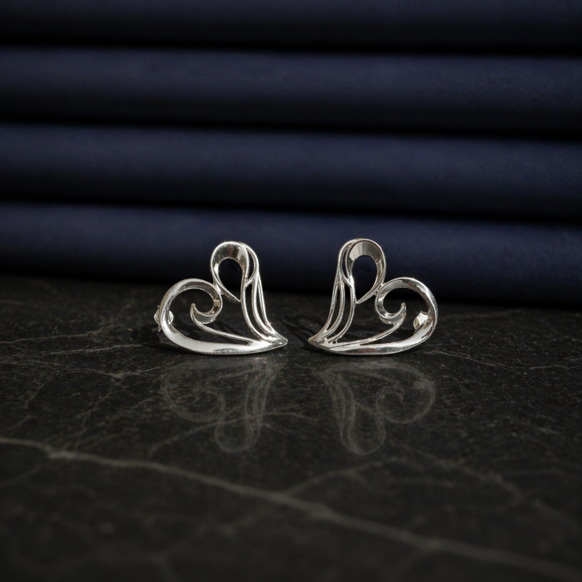 Front view of the Trueform Heart in Studs on a dark marble surface, showing the delicate wired open heart design in rhodium-plated 925 sterling silver.