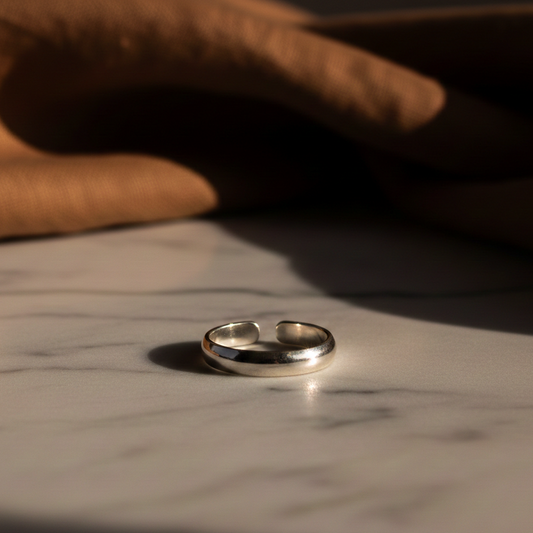 Minimal silver band ring placed on a marble surface with warm natural light, showcasing a sleek and timeless design.