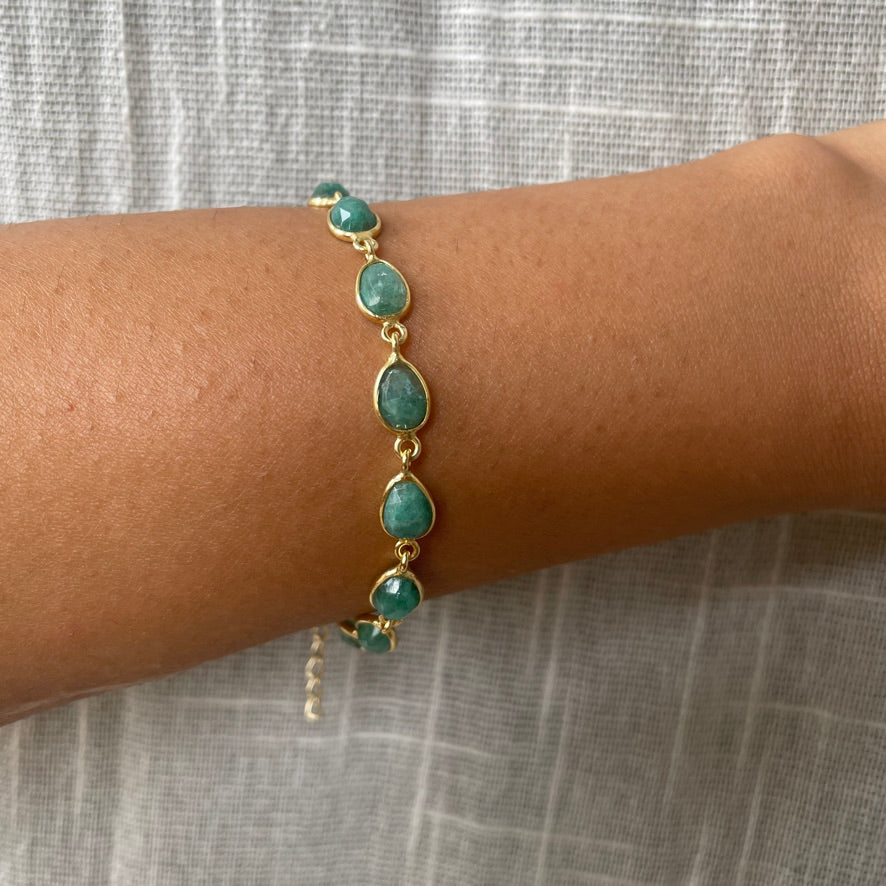 A close-up view of a wrist wearing a dainty link bracelet adorned with smooth, oval-cut green beryl stones.