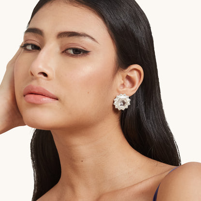 A portrait of a model showcasing a silver floral stud earring with a light pink faceted stone against dark hair.