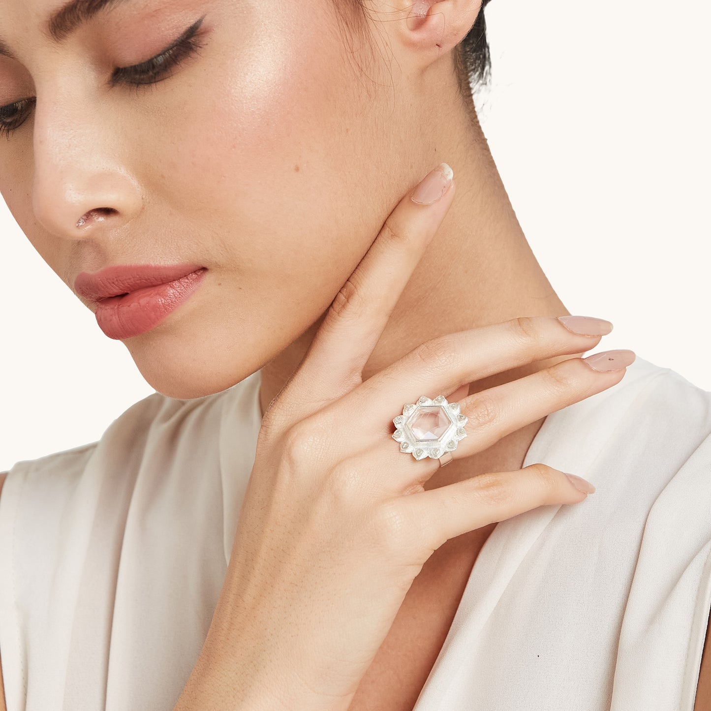 A woman in a white top posing with her hand near her neck, showcasing a silver ring with a pale pink hexagonal gemstone.