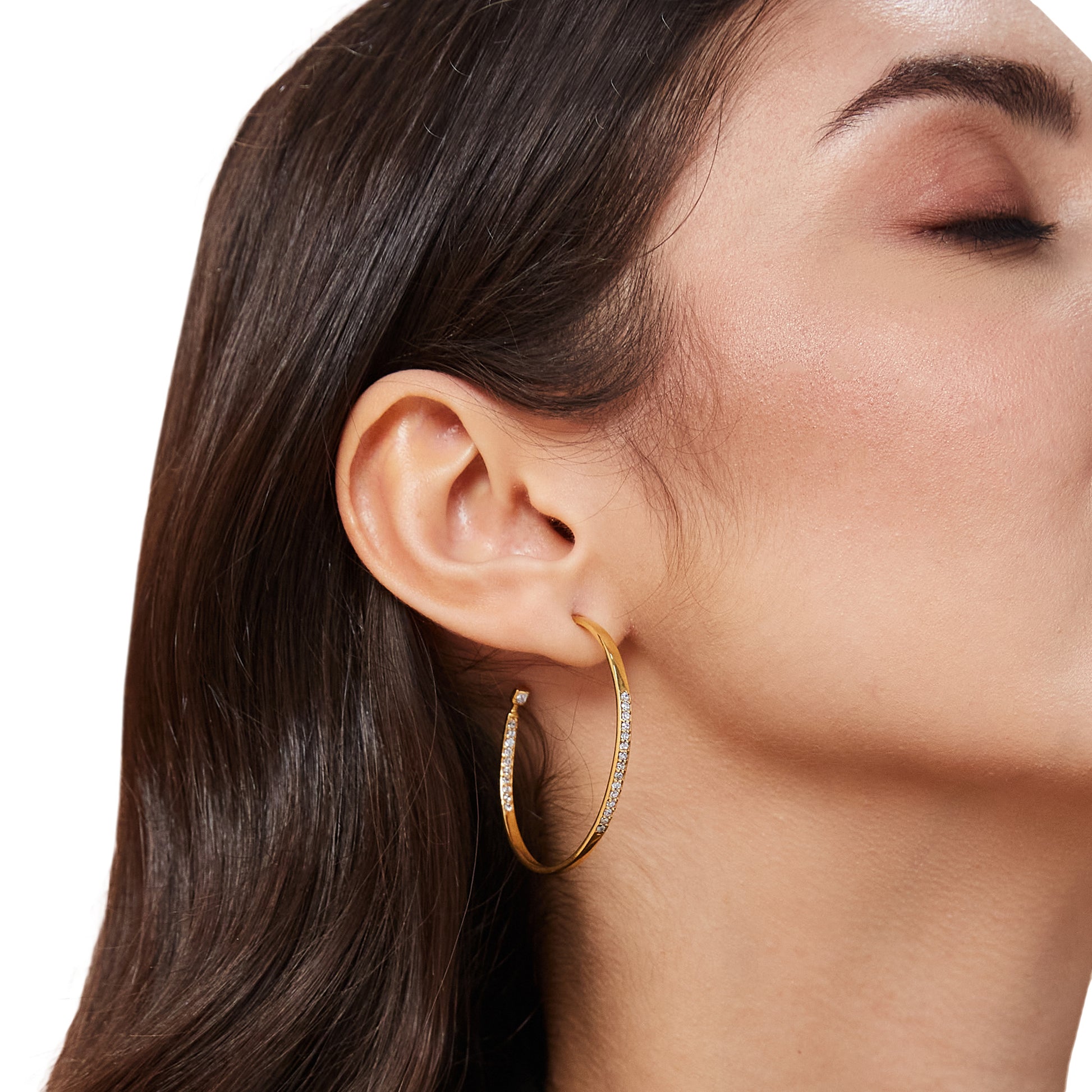 A side profile of a model wearing chunky gold huggie earrings that feature a distinct, hammered-texture surface.