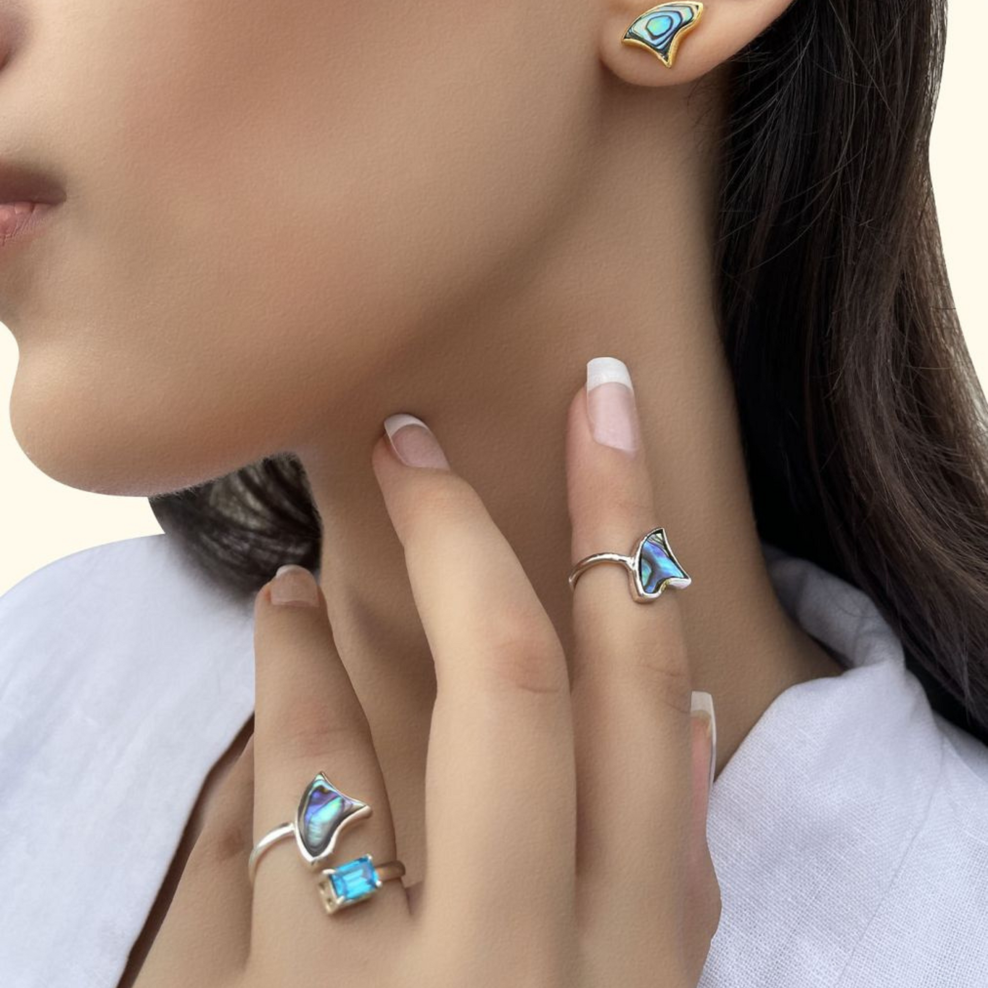 A side profile of a model wearing an open-style silver ring with an iridescent abalone shell inlay and a blue gemstone, paired with matching abalone shell stud earrings.