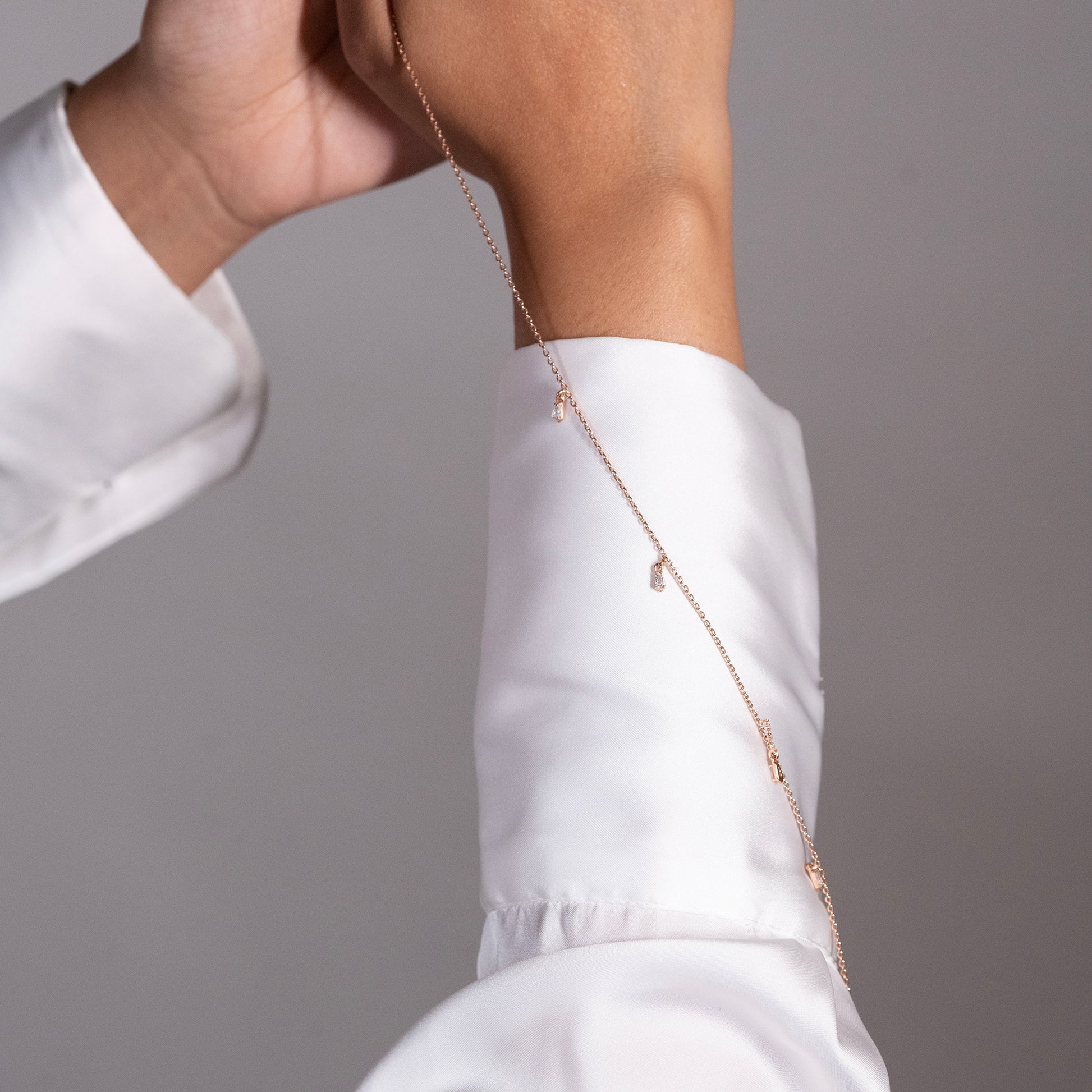  A dainty rose gold chain with subtle, evenly spaced embellishments that add a touch of warm, understated glamour on a model's wrist.