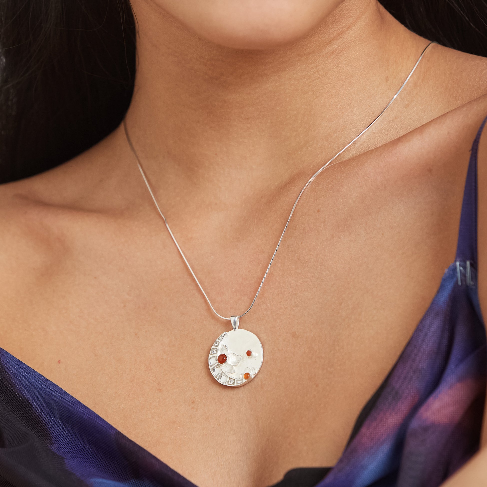 Close-up shot of a model wearing a unique, artisanal sterling silver Full Moon pendant with gemstone accents.