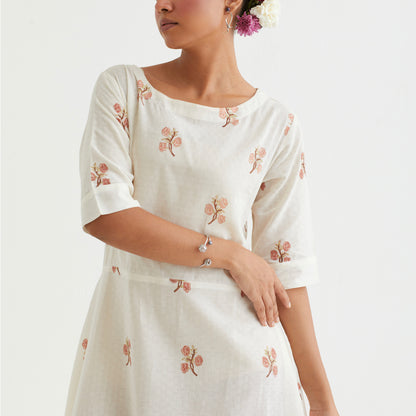 A person wearing a long, floral-patterned dress and a simple, open-style metal bracelet with spherical embellishments on their wrist.