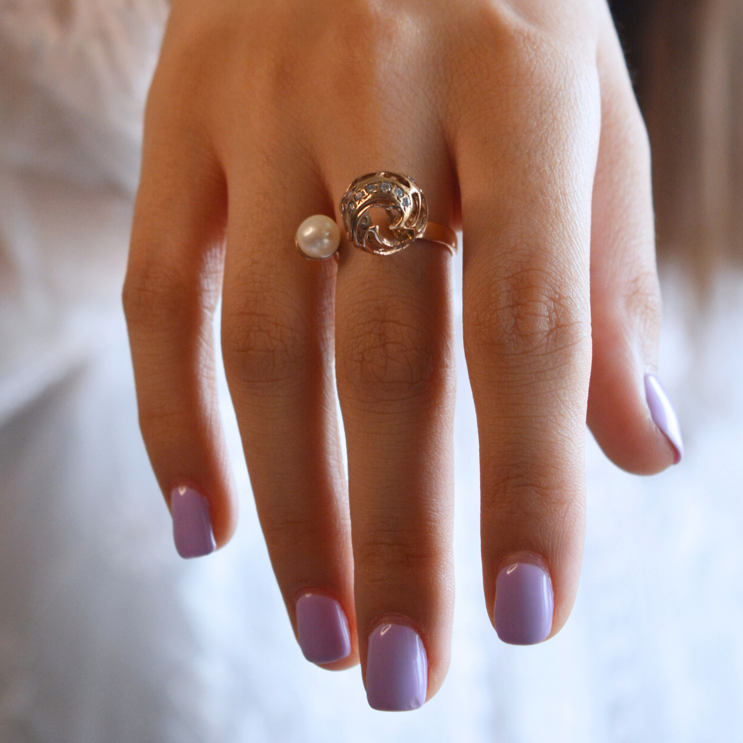 A lifestyle shot of a hand wearing a modern rose gold pearl ring, highlighting the contrast between the metallic copper tones and the soft white pearl.