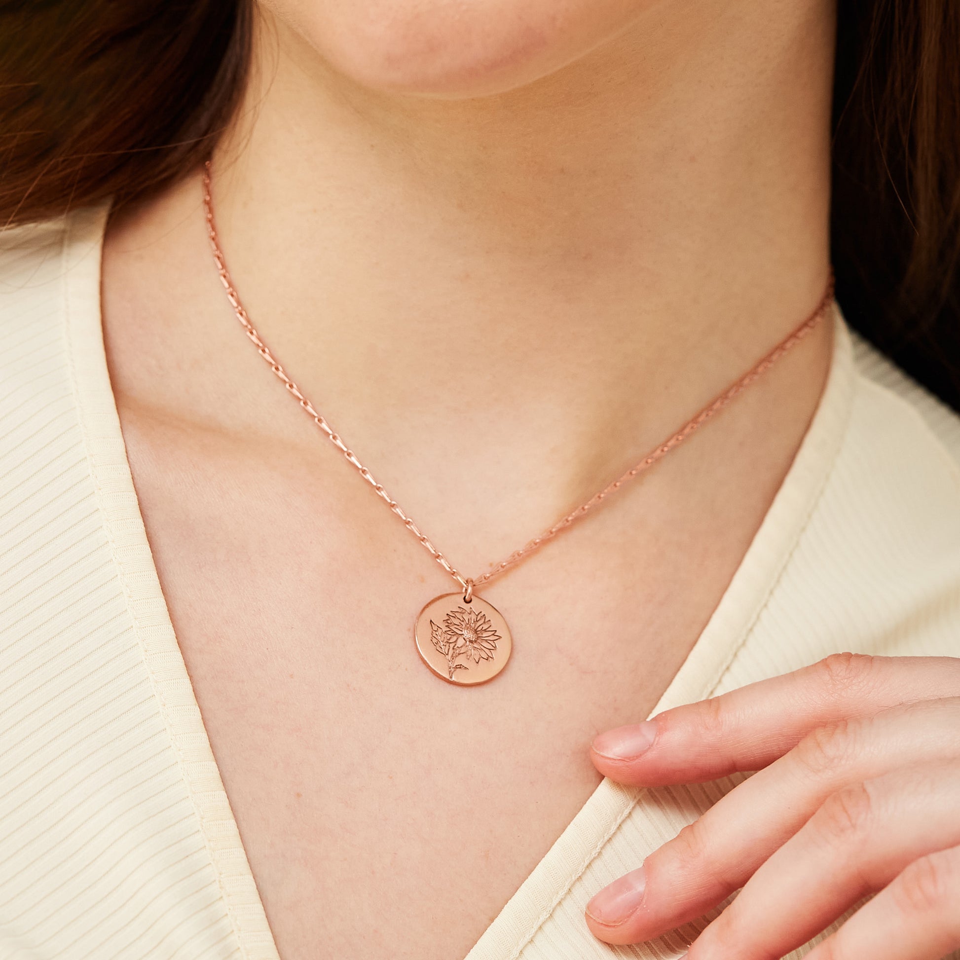 Close-up of a model showcasing the detailed sunflower engraving on a rose gold medallion pendant necklace.