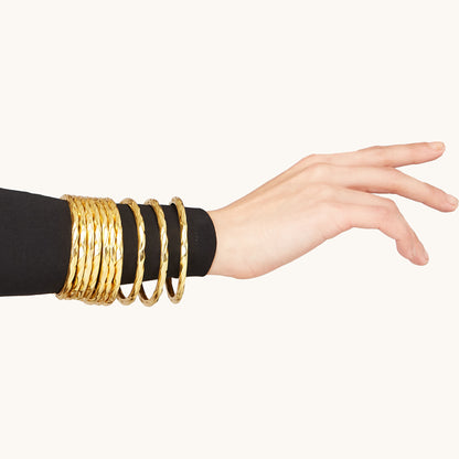 A close-up portrait of a woman wearing a minimalist circular metallic bangle on her wrist.