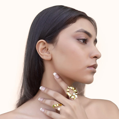 A model showcasing an asymmetrical, flowing gold-toned metal band with a smooth, polished finish worn on the ring finger.