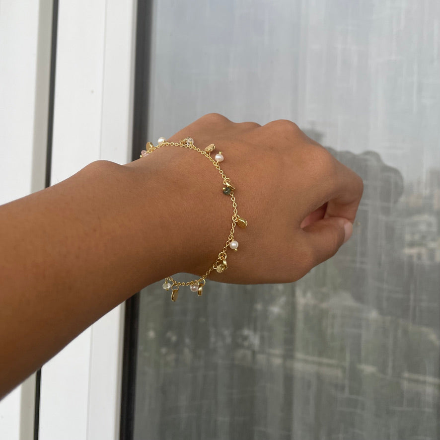 A wrist shot showing a gold-plated silver chain bracelet with dangling pearls, gemstone beads, and gold discs.
