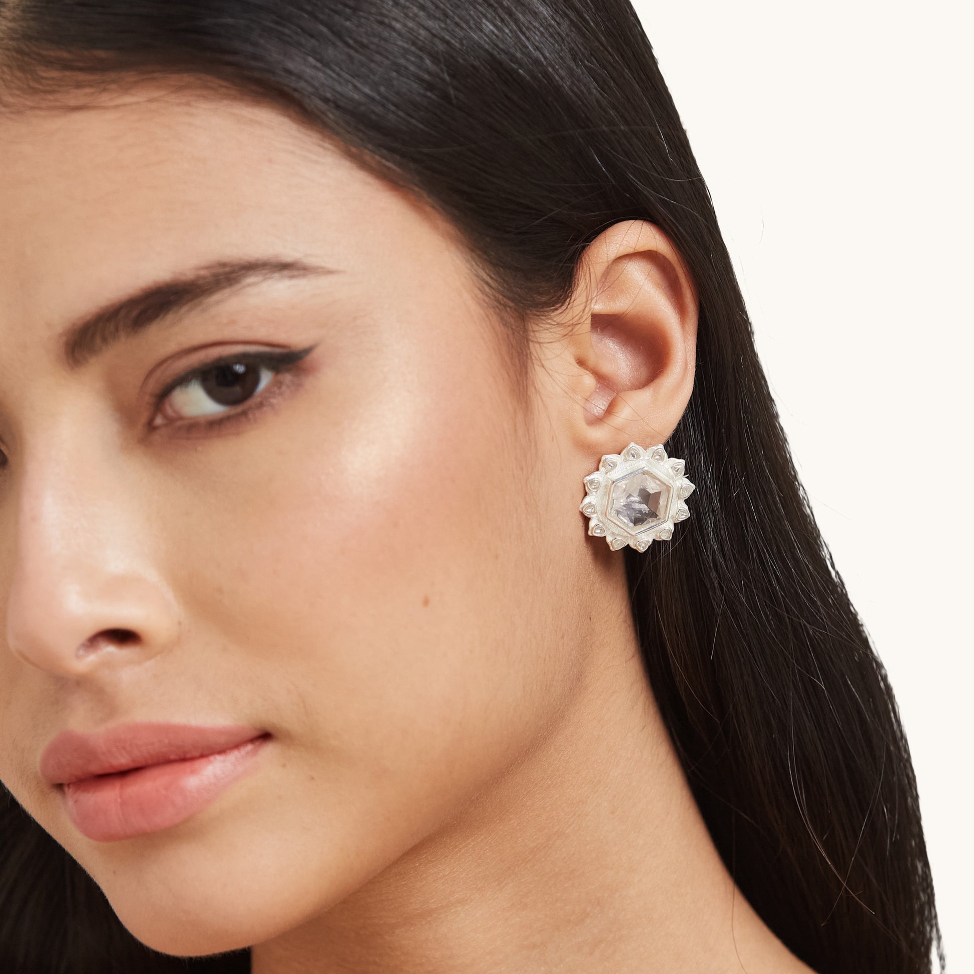 A profile view of a model wearing a minimalist silver stud earring with a hexagonal pink stone and petal-shaped silver border.