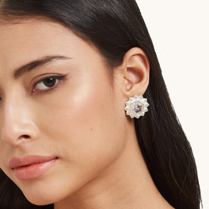 A profile view of a model wearing a minimalist silver stud earring with a hexagonal pink stone and petal-shaped silver border.