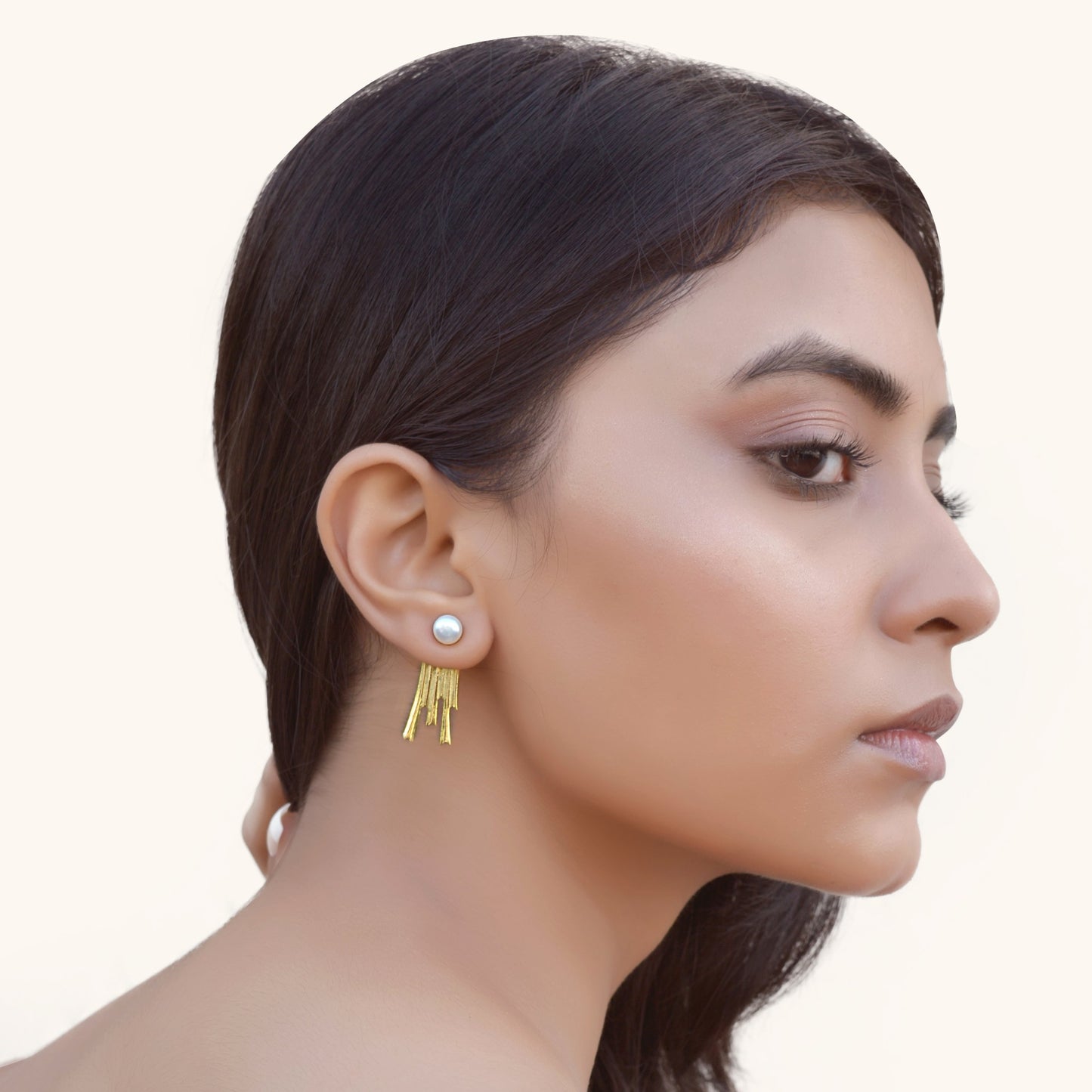 Side profile of a model showcasing the length and movement of a gold tassel earring jacket paired with a white pearl.