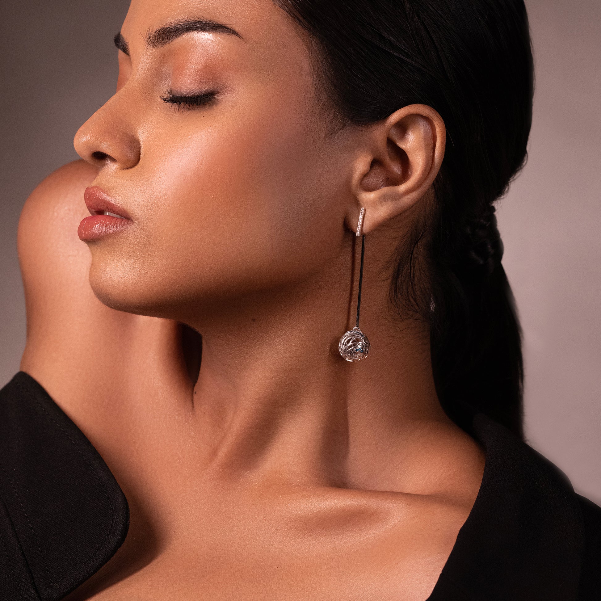 Close-up of a silver multi-tiered drop earring with blue stone accents and delicate filigree patterns, showcasing a sophisticated platinum-plated finish.