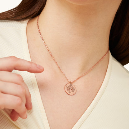 A model's hand gently touching a rose gold Sunflower Medallion necklace, emphasizing the jewelry's elegant design and texture.