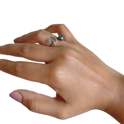 An elegant hand wearing a wave-inspired silver ring with a tranquil blue pearl, highlighting its adjustable fit and refined, ocean-inspired aesthetic.