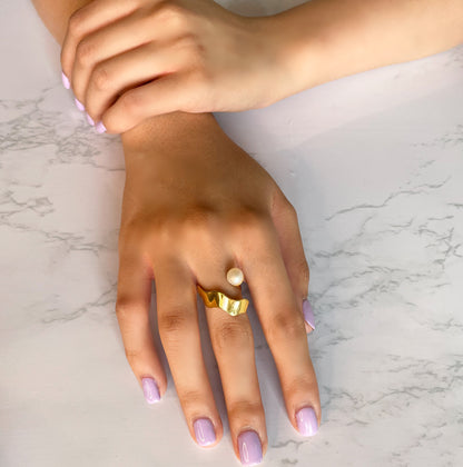 A close-up view of an elegant, sculptural gold-toned band featuring a fluid, undulating silhouette that mimics the gentle motion of a wave.