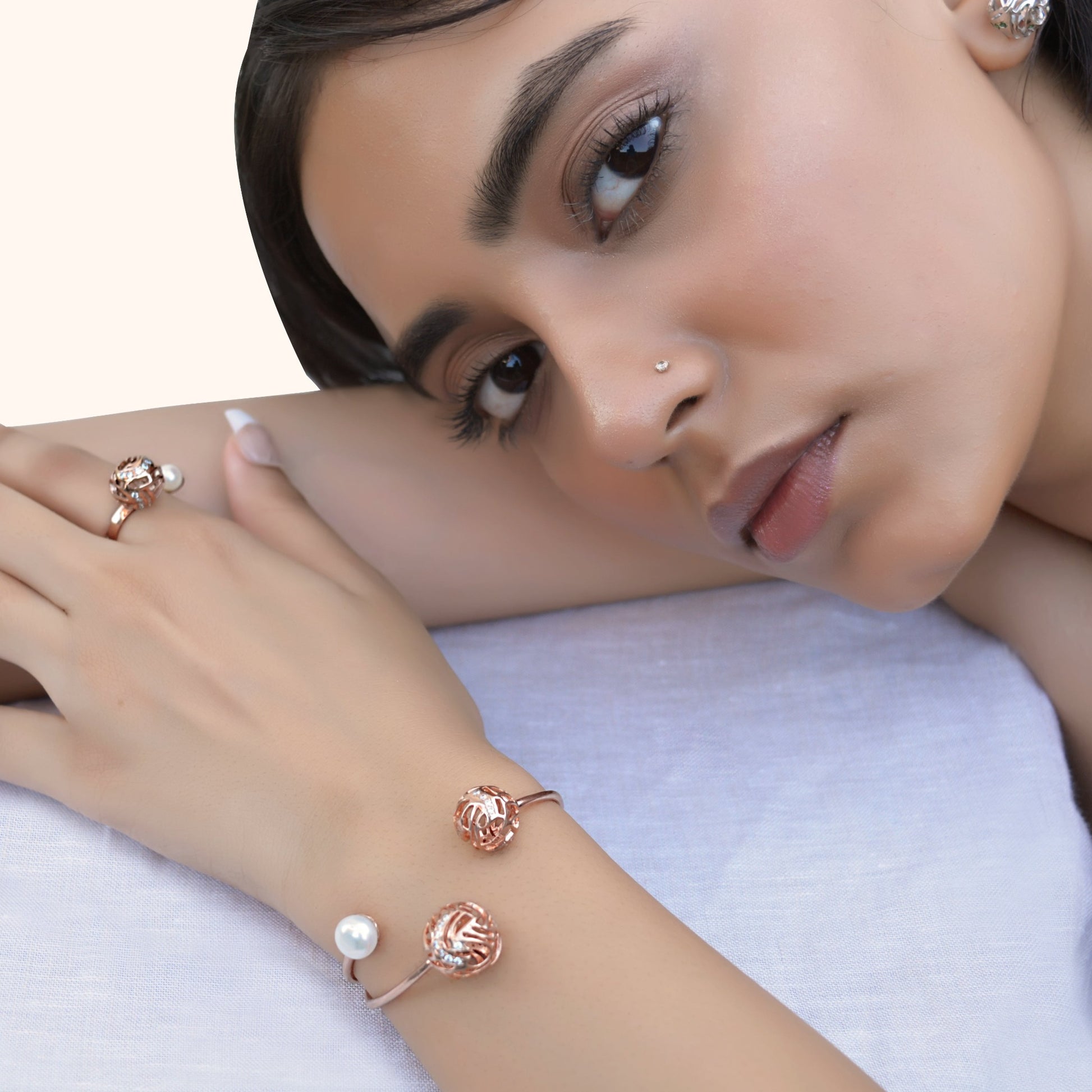 Close-up of a person resting their head on their arm, wearing a rose gold open-style bracelet with filigree spheres and a pearl.