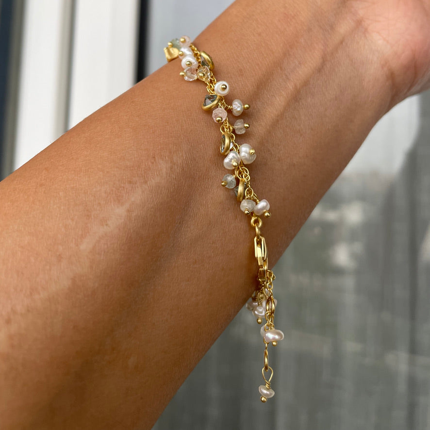 A close-up of a wrist wearing a fine double-chain bracelet adorned with dangling gemstone and pearl charms.