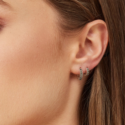Close-up view of dainty silver snuggie hoops with black stones worn on a model's ear to show size and scale.