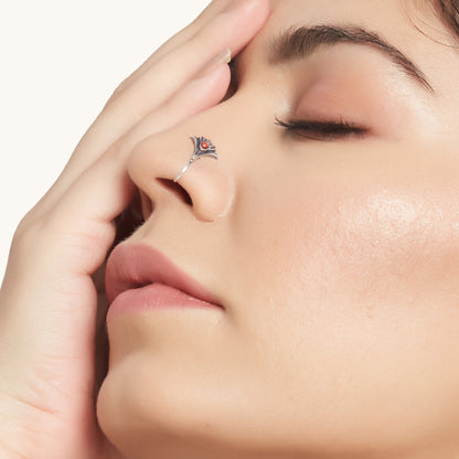 A close-up profile shot of a person wearing an intricate, silver-toned nose clip-on featuring a warm, reddish-orange stone in the center.