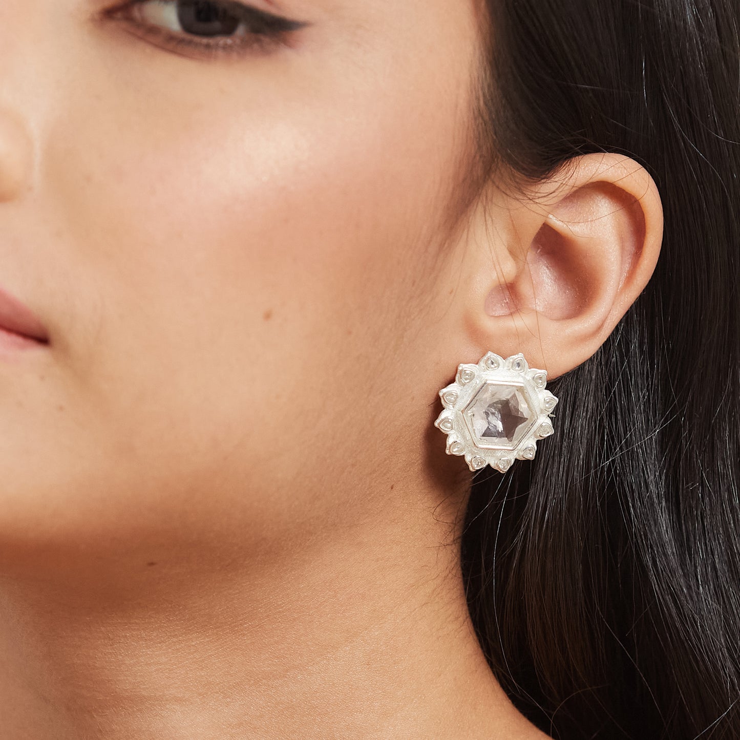 A close-up of a person's ear wearing a silver floral stud earring with a translucent pink hexagonal gemstone centerpiece.